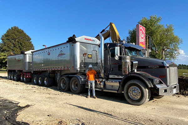 Image of Doug Paschall standing beside his semi-truck trailer end dump on a work site. 